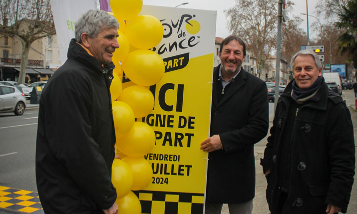Photo de 3 hommes, dont le maire d'Agen, qui sourient à la caméra, en présentant une pancarte du Tour de France accompagnée de ballons jaunes